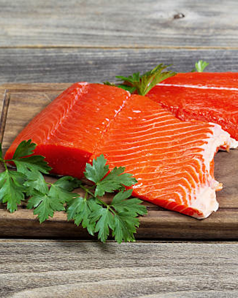 Horizontal photo of fresh raw red salmon fillet on traditional wooden server with parsley on the side and rustic wood underneath